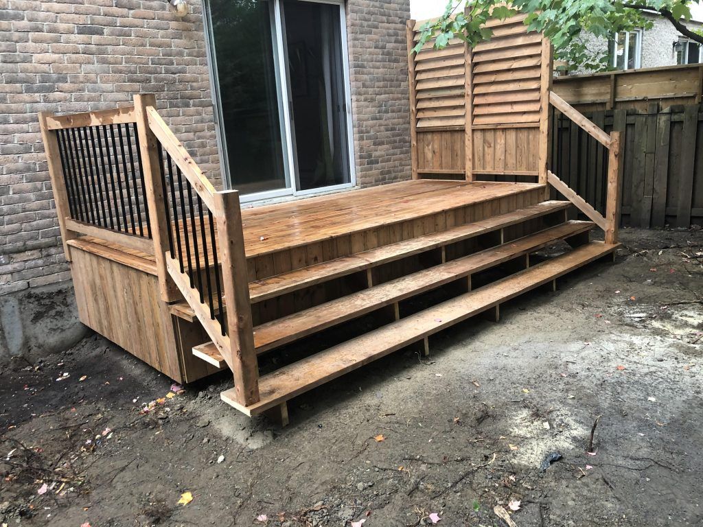 Une terrasse en bois avec escalier et balustrade devant une maison en briques.