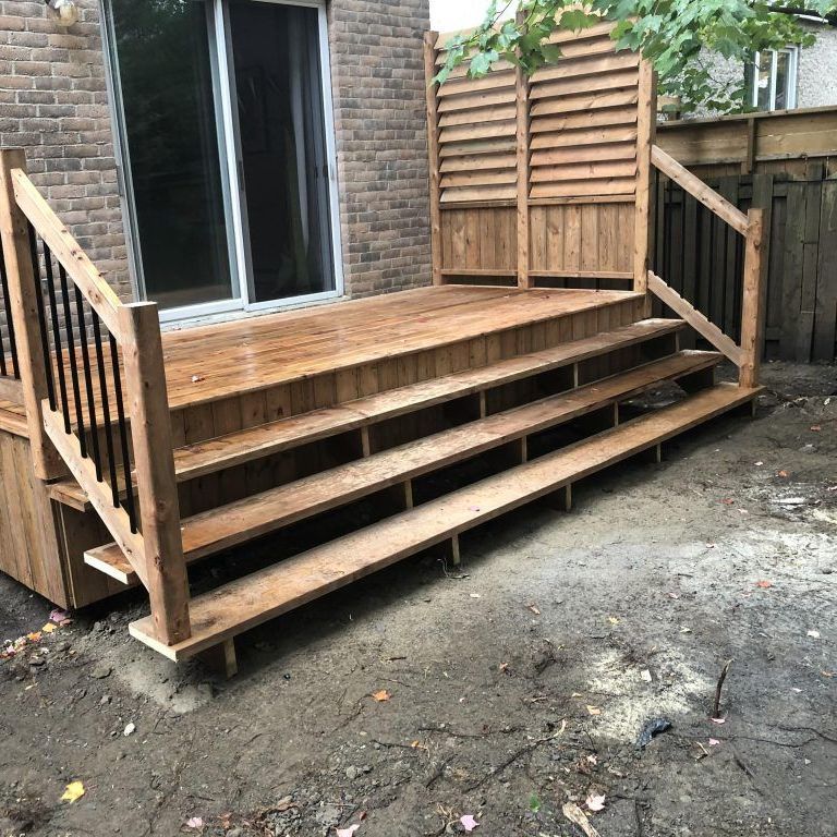 Une terrasse en bois avec des escaliers et un bâtiment en briques en arrière-plan