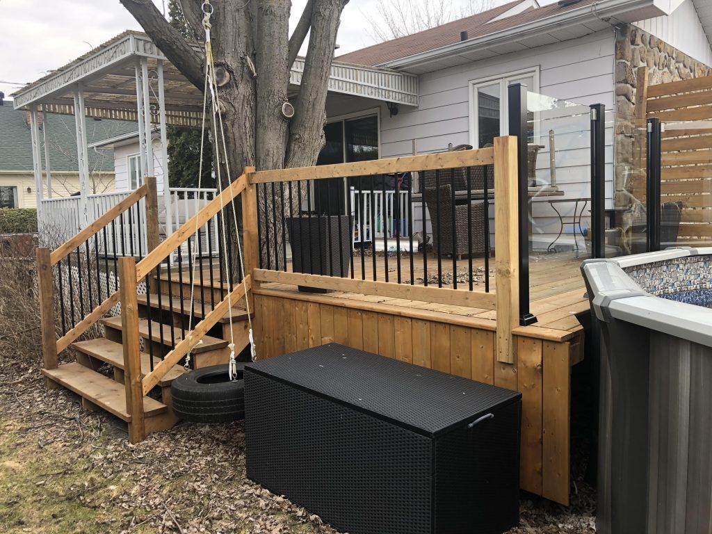 Une terrasse en bois avec des escaliers et une boîte noire devant une maison.