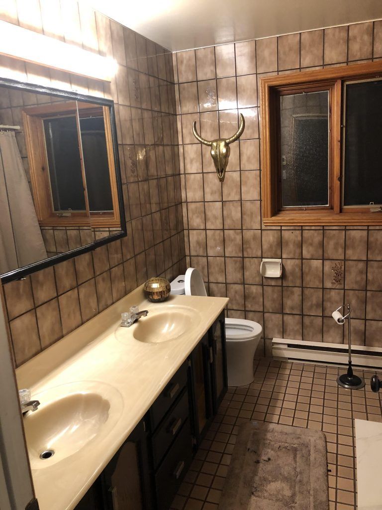 Une salle de bain avec deux lavabos, un WC, un miroir et une tête de taureau au mur.