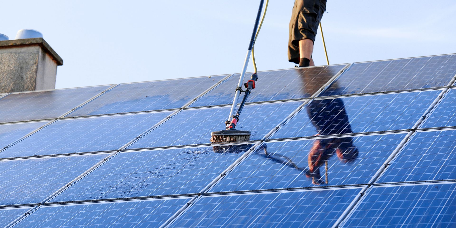 A man is standing on top of a roof cleaning solar panels.