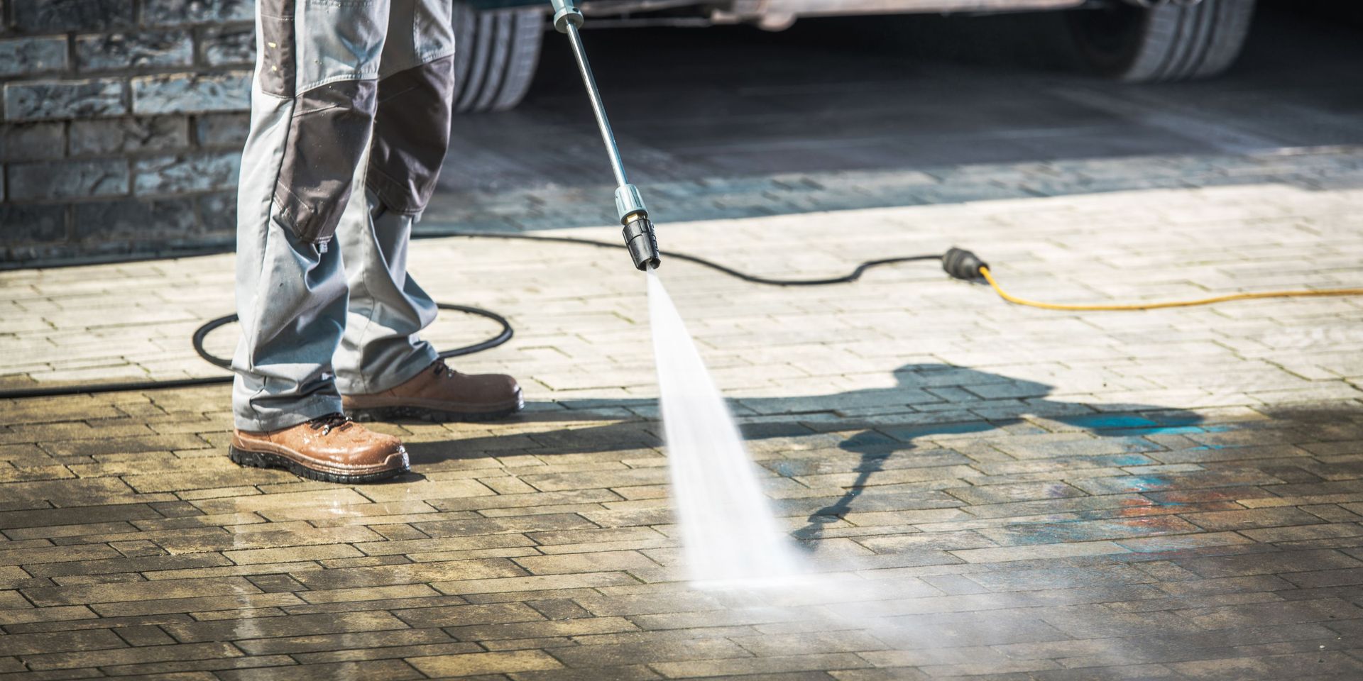 A man is using a high pressure washer to clean a brick driveway.