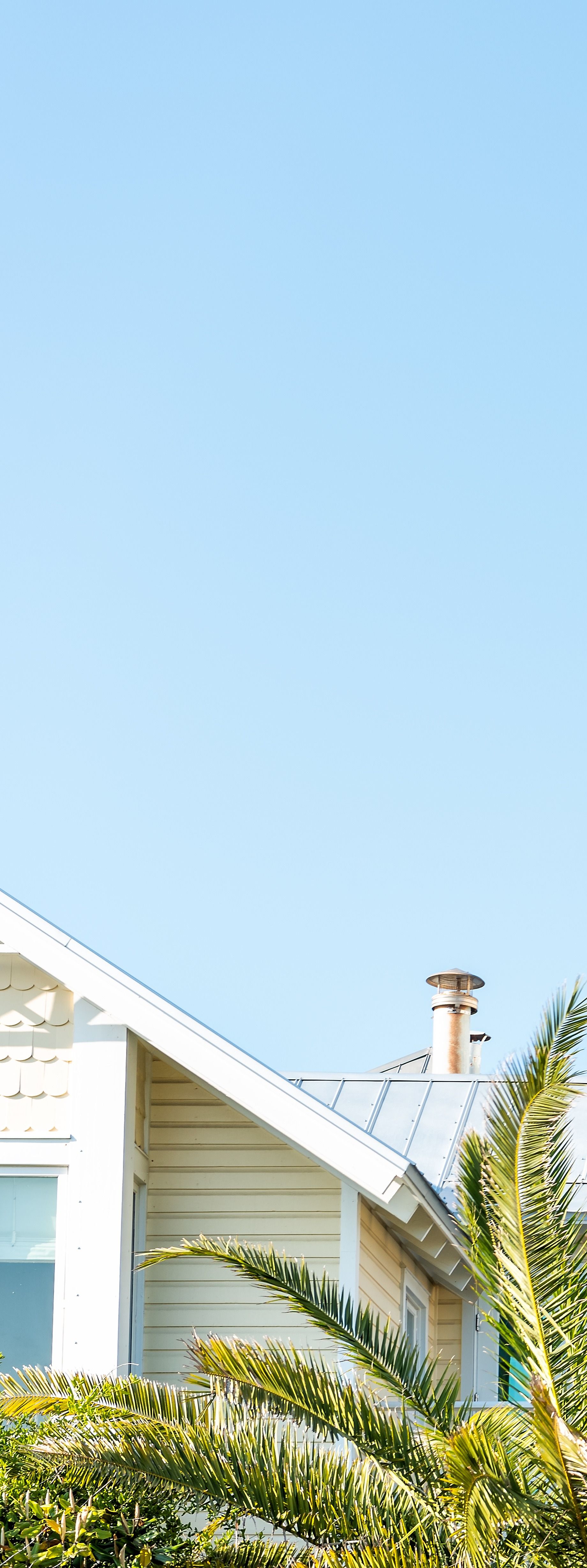 Sky above a building's roof and chimney with green foliage in front.