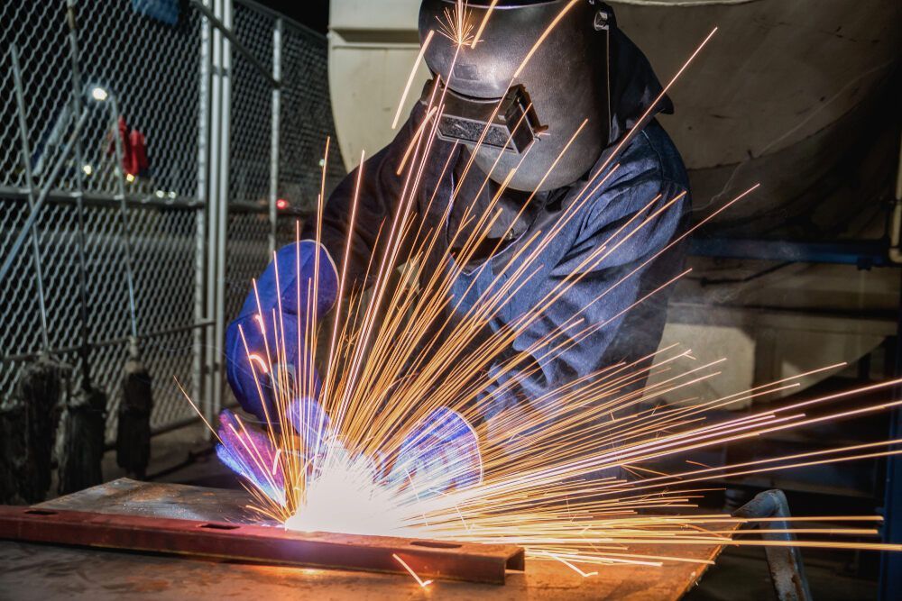 A Man Is Welding A Piece Of Metal In A Factory — JA Toft & Co In Bundaberg Central, QLD