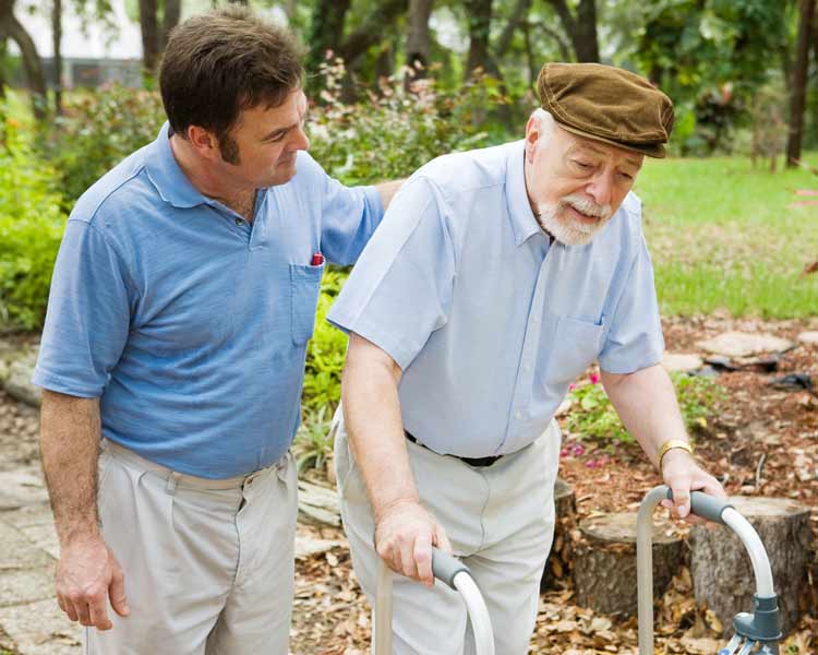 Personal trainer helping elderly man walk outdoors