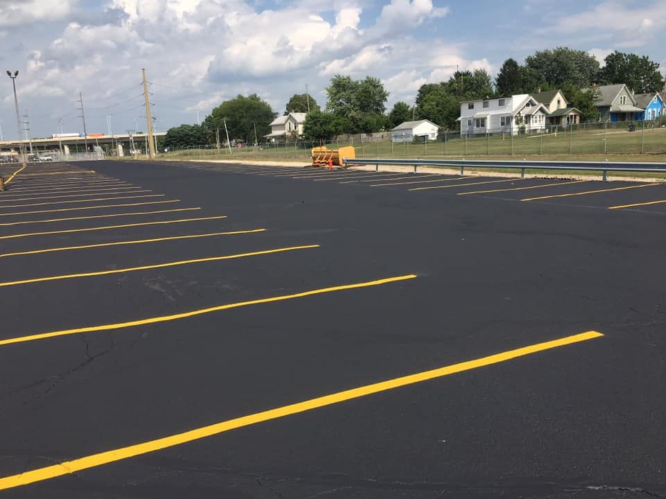 Newly paved parking lot with yellow parking space lines. Houses and trees are in the background.