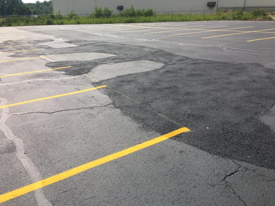 Parking lot with cracked asphalt, partially resurfaced with dark pavement and yellow parking lines.