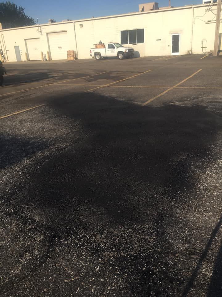 A parking lot with a pickup truck in front of a white building. The asphalt has patches and is sunlit.