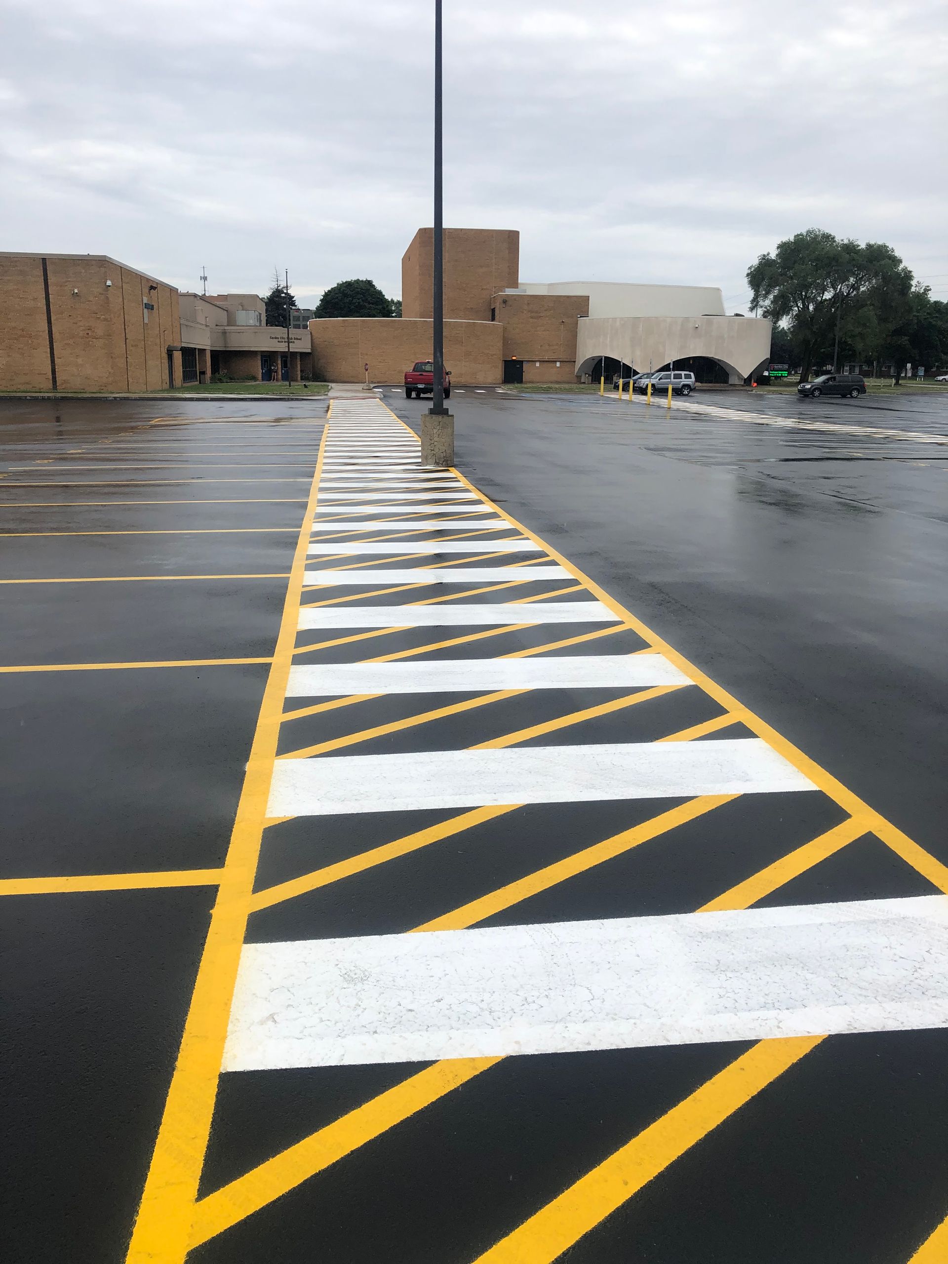 Yellow and white striped pavement marking leading toward a building in a wet parking lot.