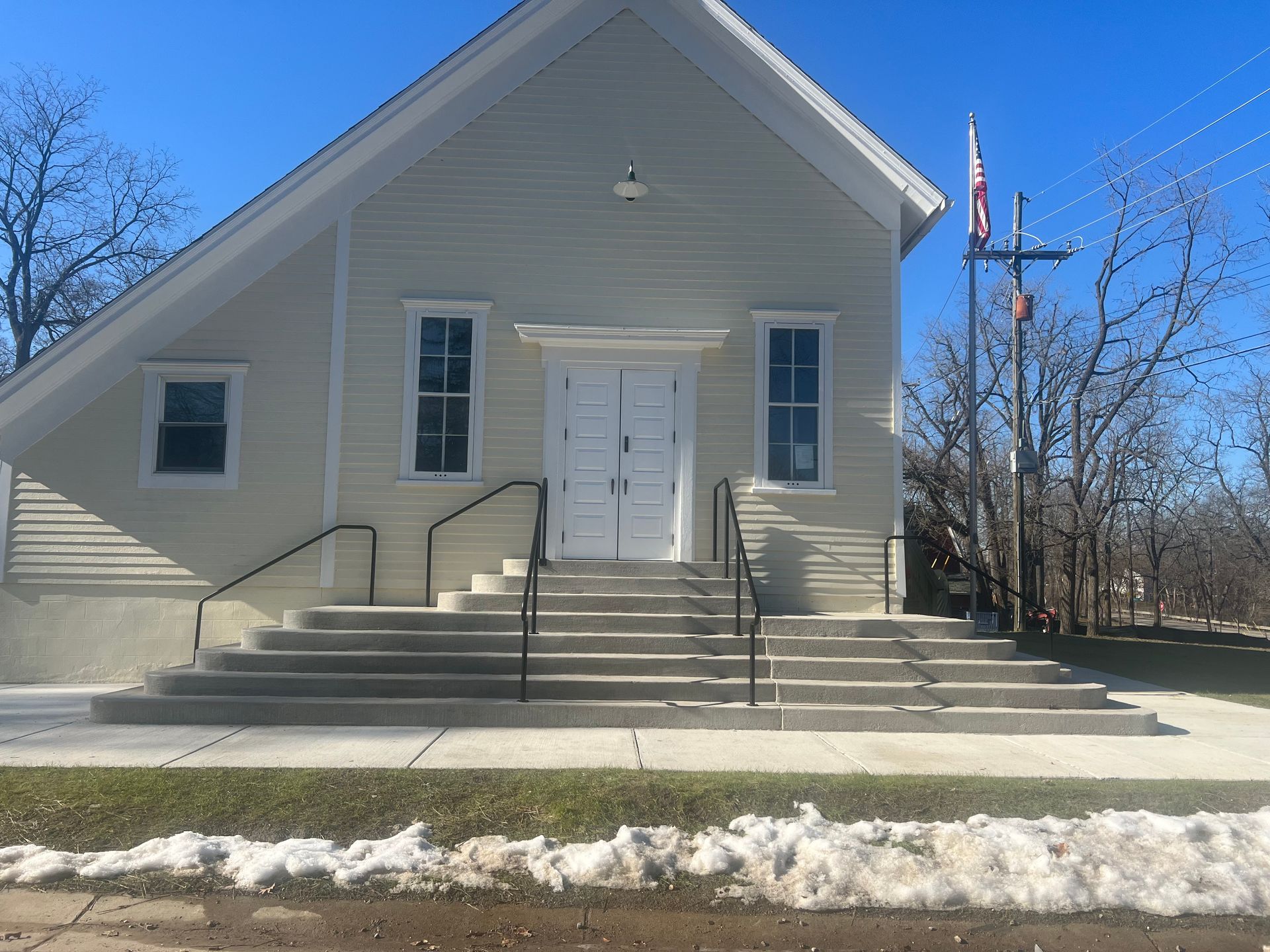 Light beige building with steps, double doors, and a cross. Snow on the ground.