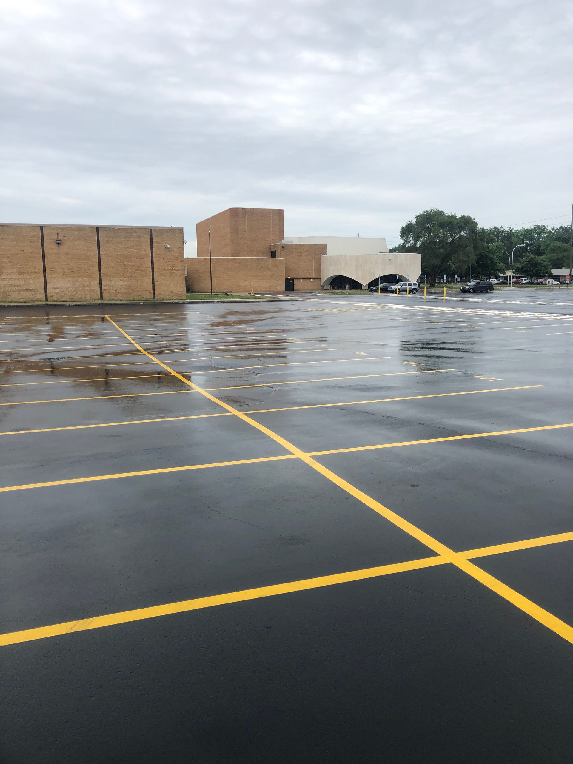 Wet parking lot with yellow lines in front of a brick building on a cloudy day.