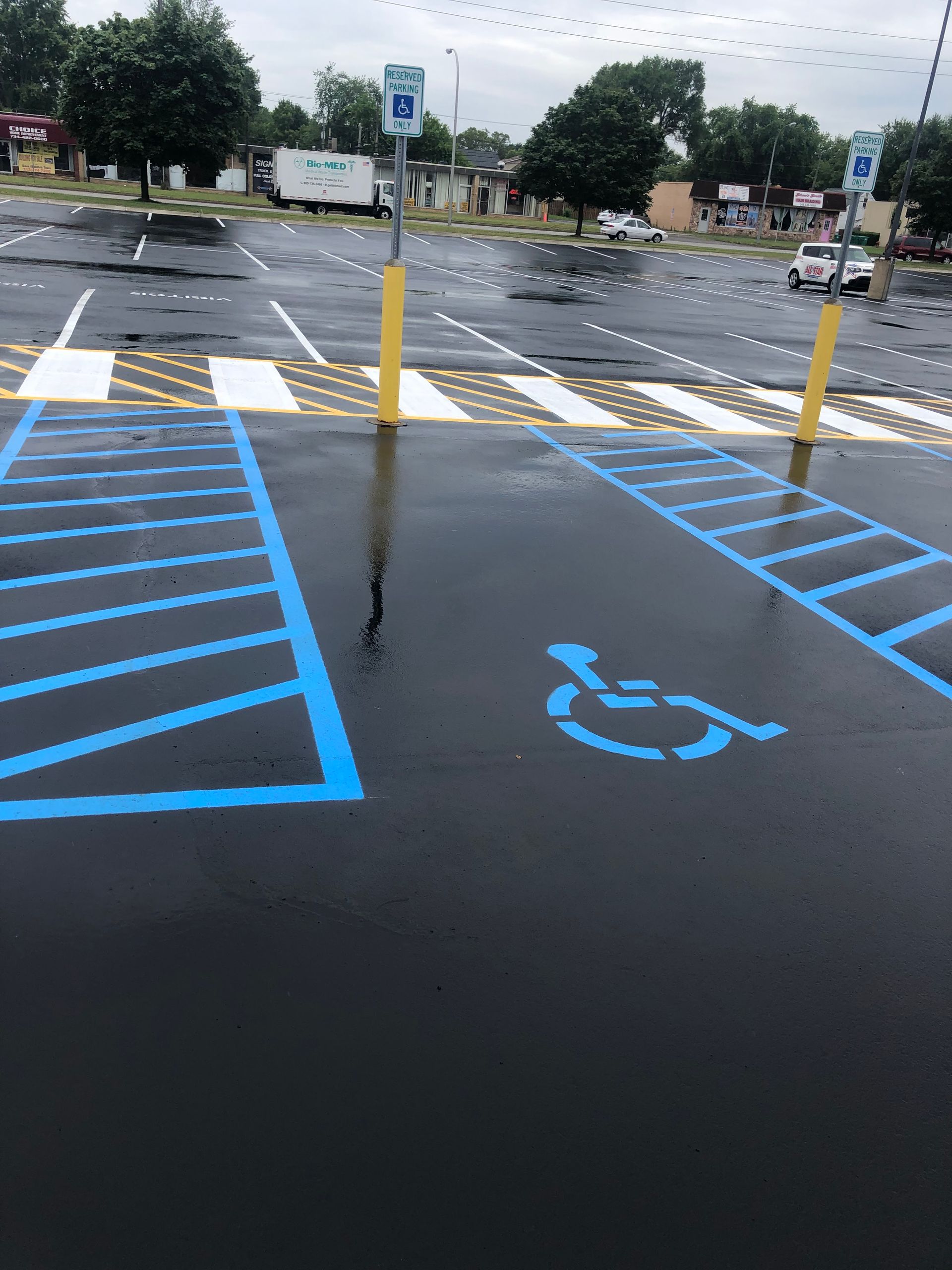 Blue painted handicap parking spaces and crosswalk in a wet parking lot.