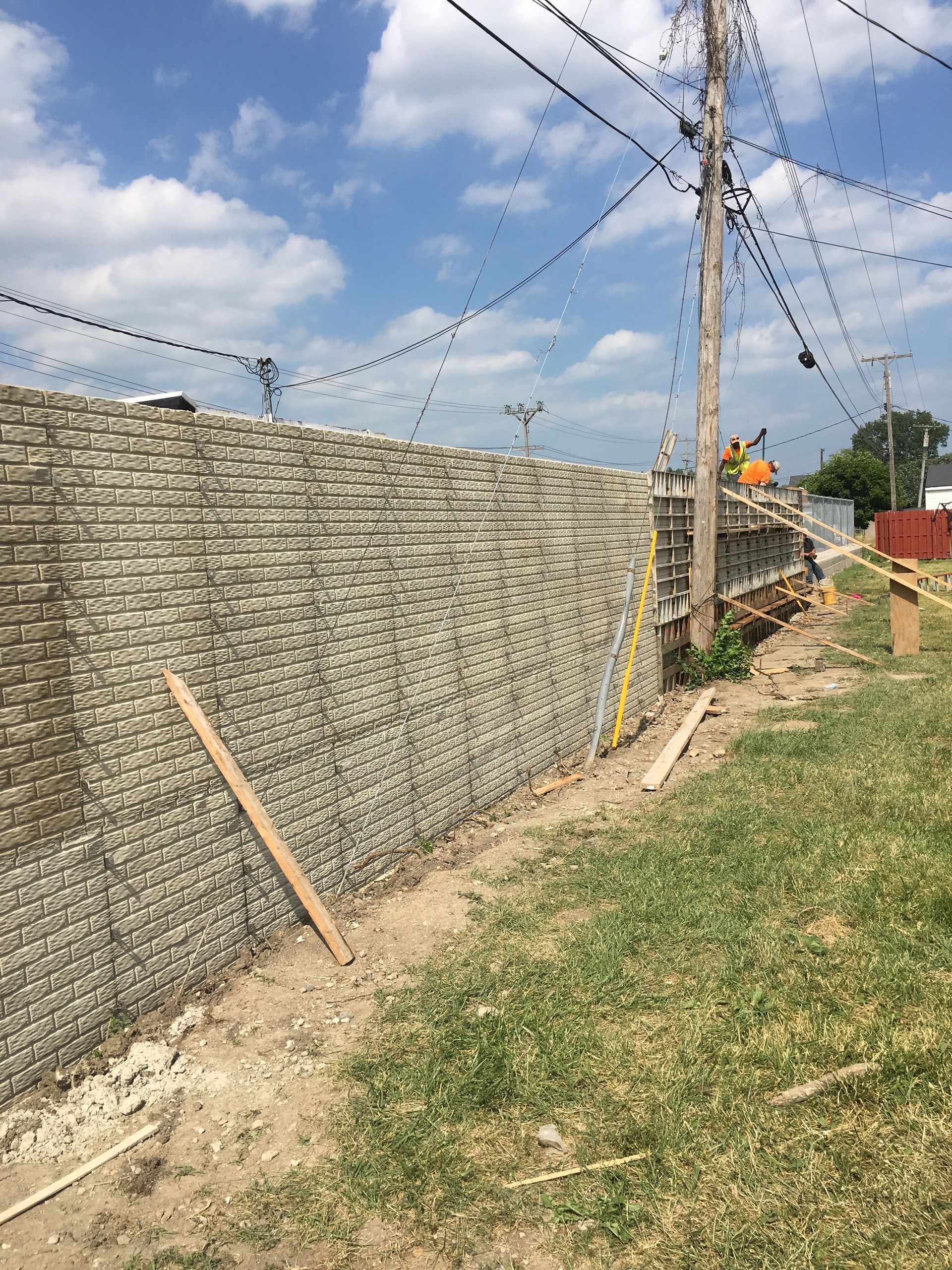 Gabion retaining wall construction along a grassy edge, with utility pole and blue sky.