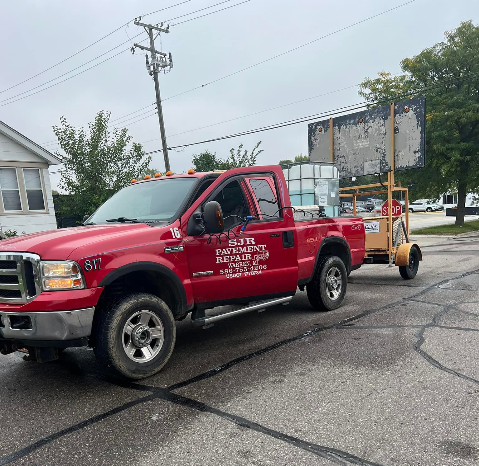 Red pickup truck with water containers, towing a light tower on a city street.
