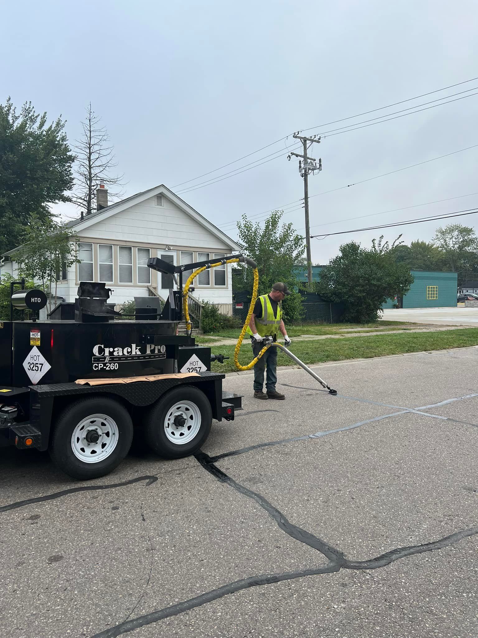 Person sealing cracks in a street with a machine in front of a house on a cloudy day.