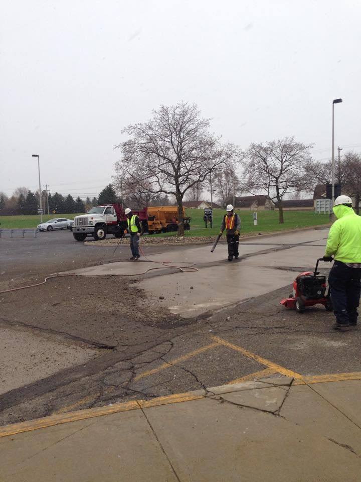 Road workers in safety vests repair asphalt parking lot on a cloudy day.
