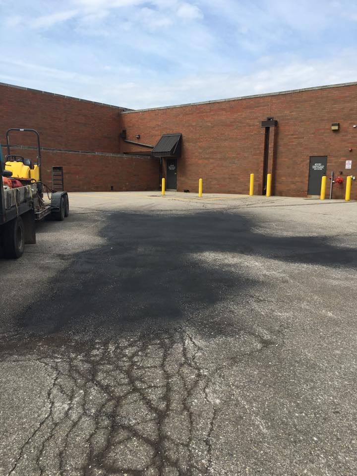 Black asphalt stain on cracked pavement in front of a brick building.