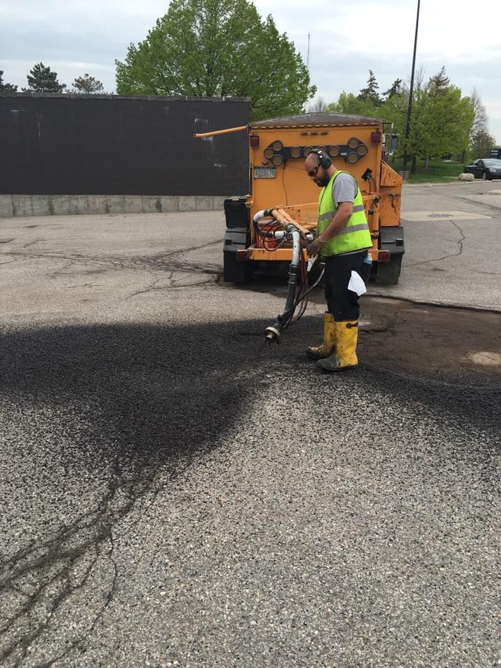 Person in safety vest using equipment to patch asphalt pavement.