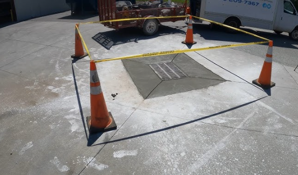 Concrete repair site, enclosed by orange cones and caution tape. Trailer and white van in the background.