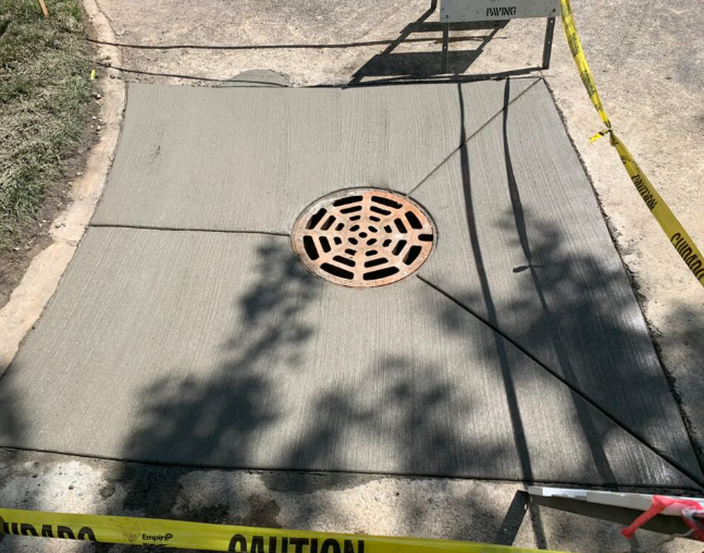 Freshly poured concrete with a drain in a walkway, surrounded by caution tape.