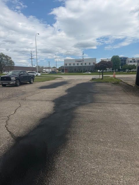 Parking lot with cracked pavement, parked cars, and a low building under a cloudy sky