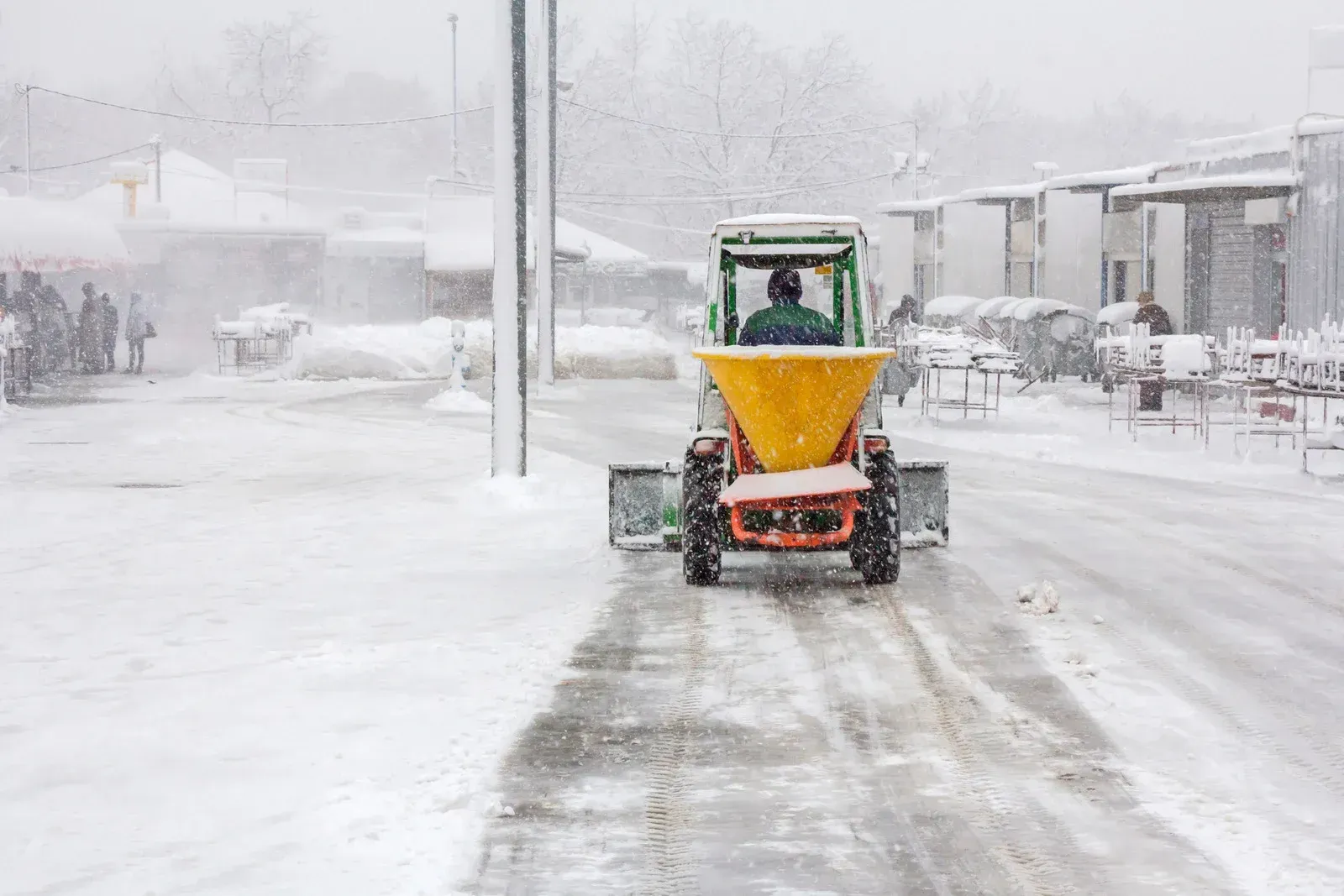 A small snowplow with salt spreader clearing a snow-covered street during a snowfall.