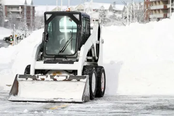 White Bobcat snowplow clearing snow from a parking lot on a snowy day.