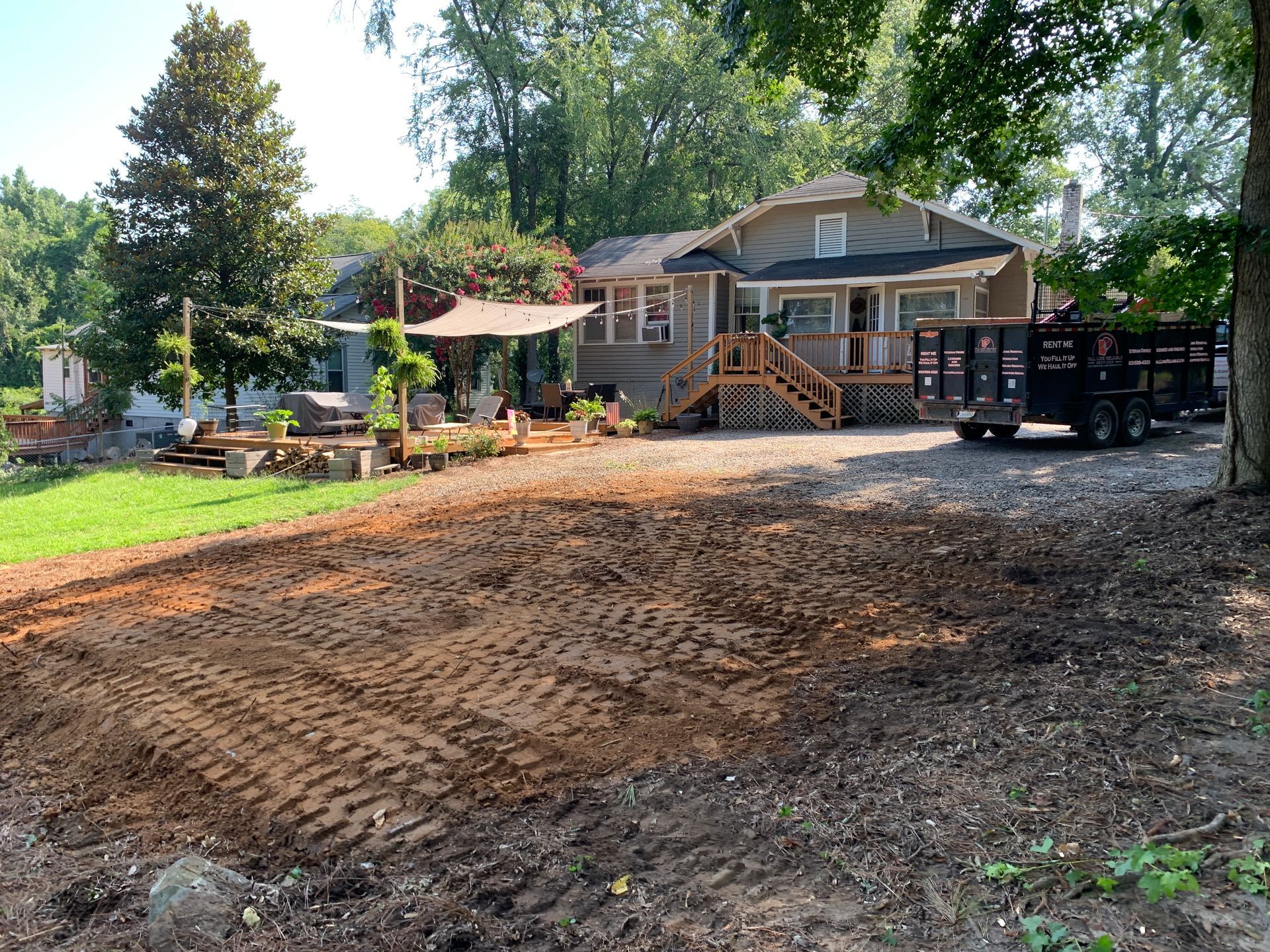 A house with a cleared yard and trailer. Beige house with porch, a brown yard with tracks.