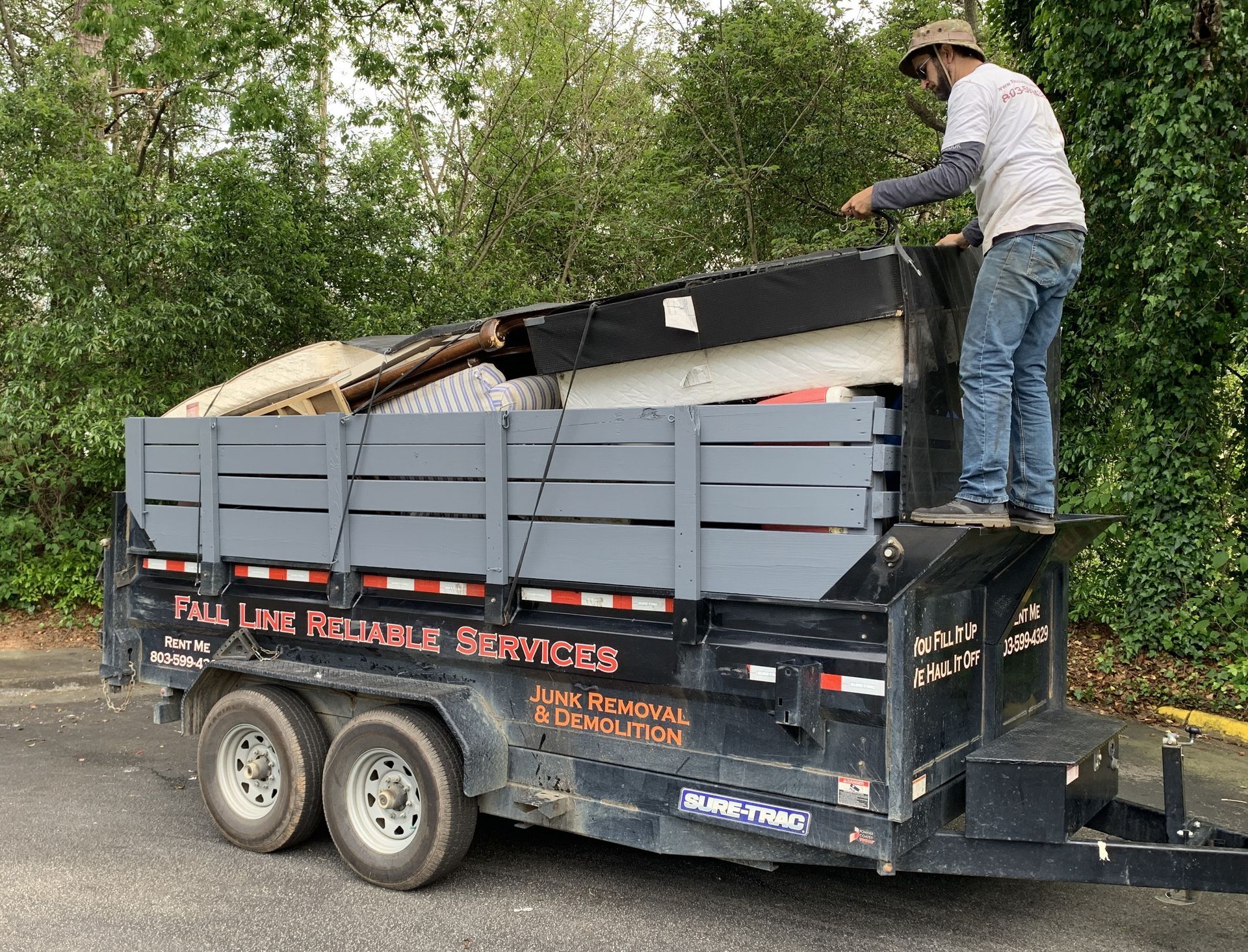 Man loading debris into a black trailer labeled 