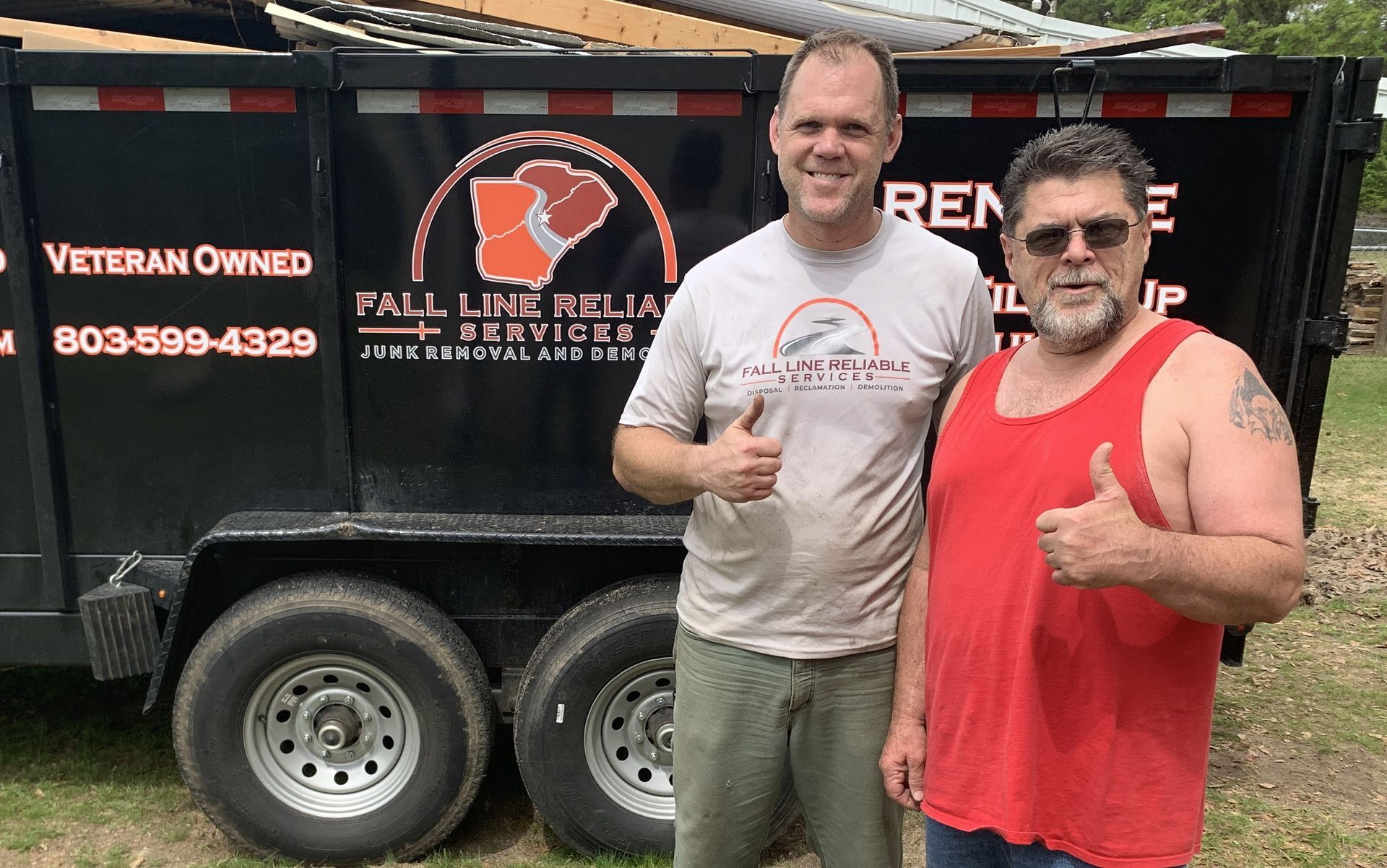 Two men giving thumbs-up next to a black trailer with 