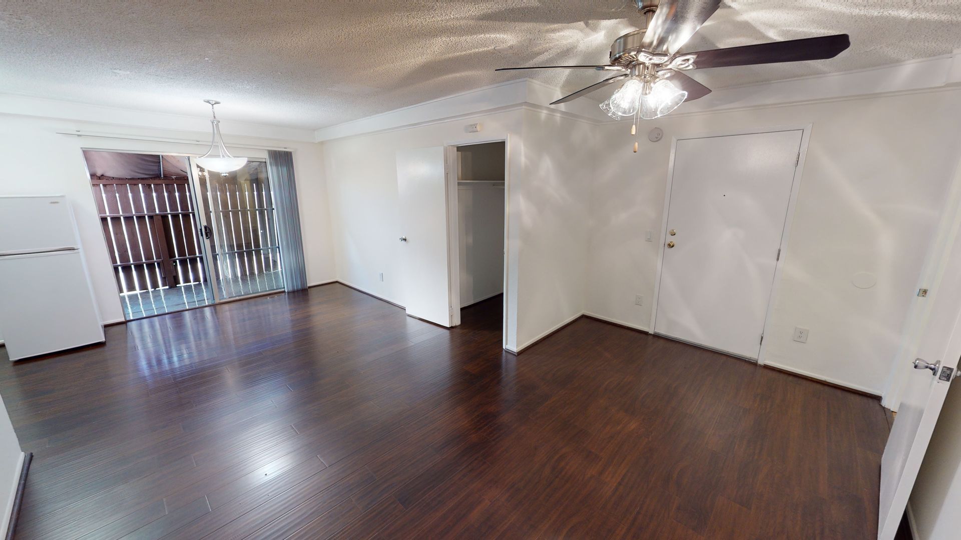 Empty living room with dark wood floor, white walls, and sliding glass door.