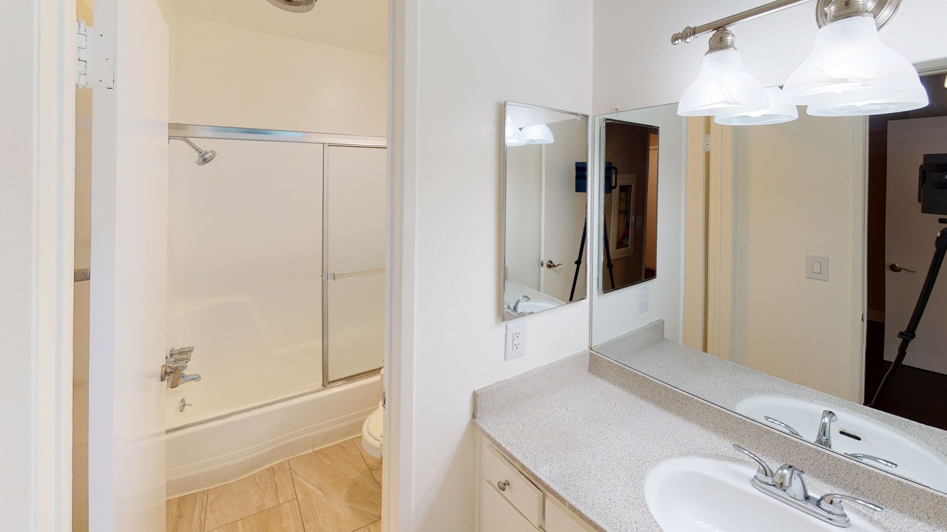 Bathroom with white sink, counter, and mirrors. Shower/tub combo in background.