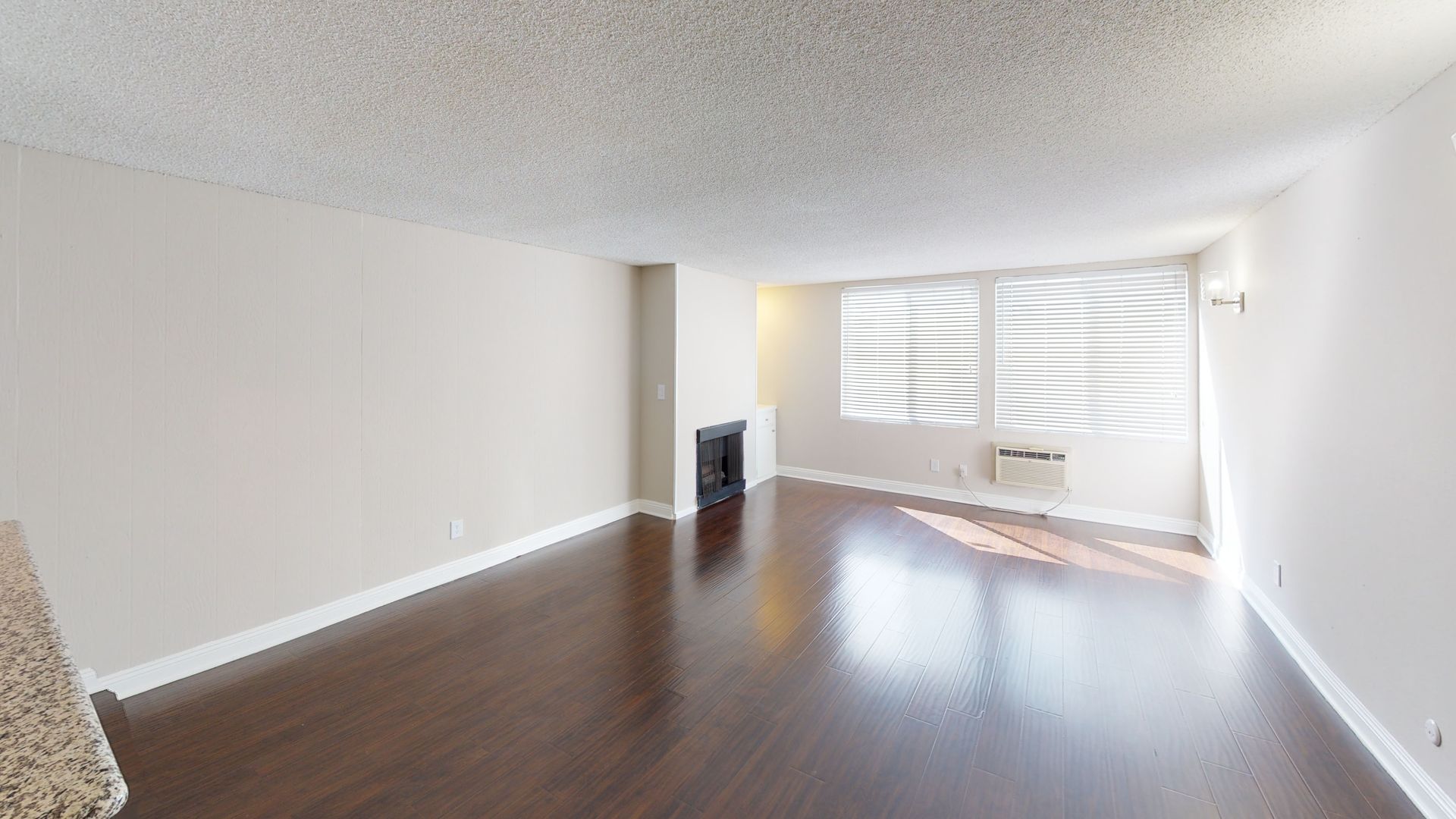 Empty living room with dark wood floor, white walls, and a window with blinds.