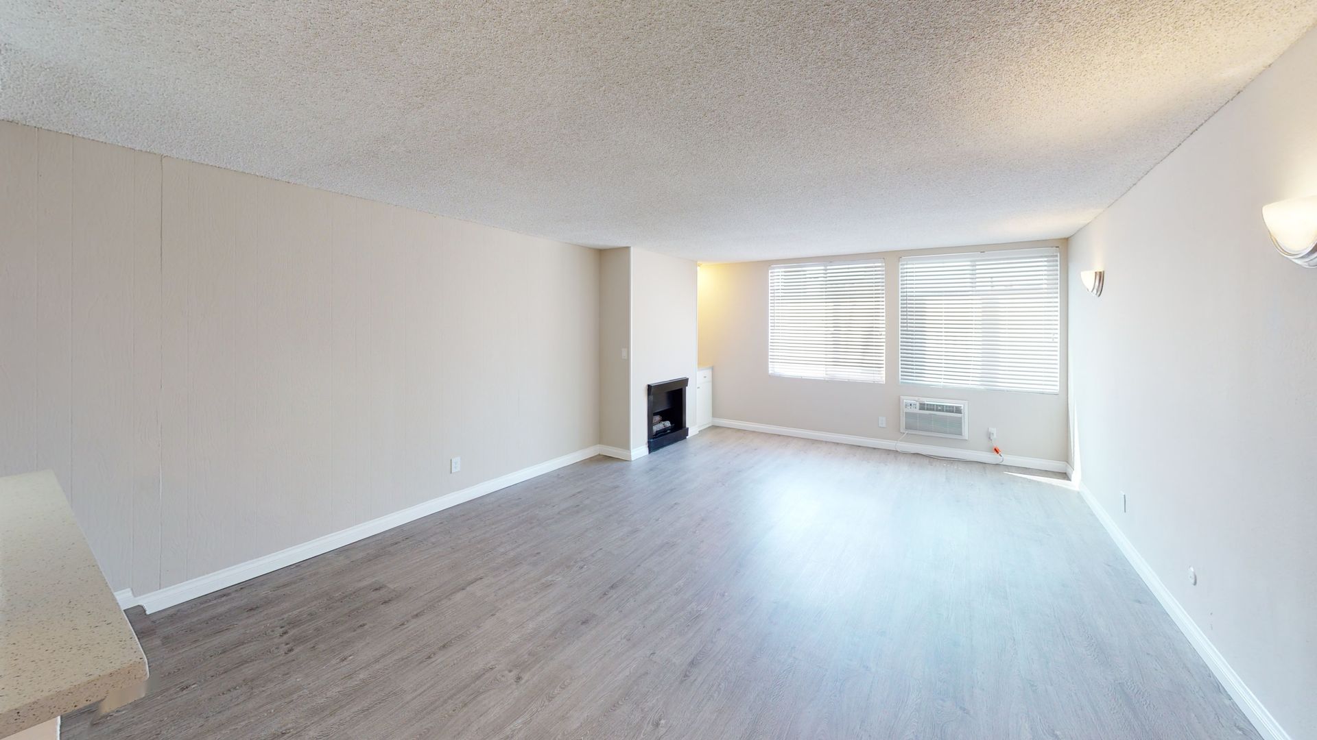 Empty living room with light gray walls, wood-look flooring, fireplace, and window with blinds.
