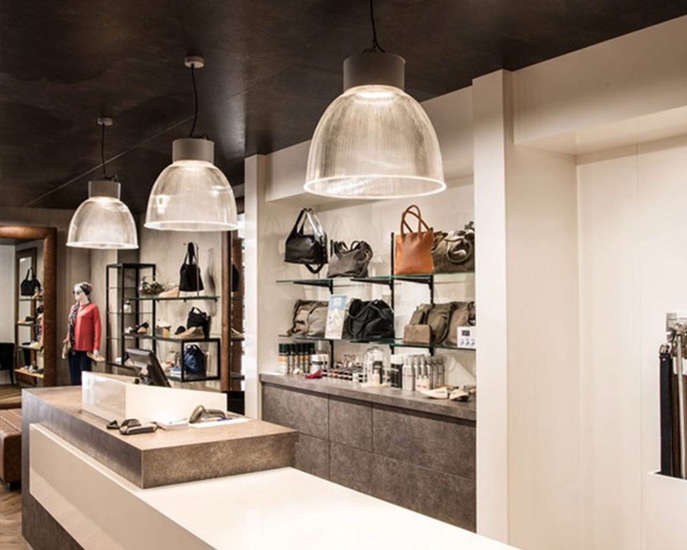 Innenansicht eines Einzelhandelsgeschäfts mit Handtaschen in Regalen, Hängelampen und einer stöbernden Frau.