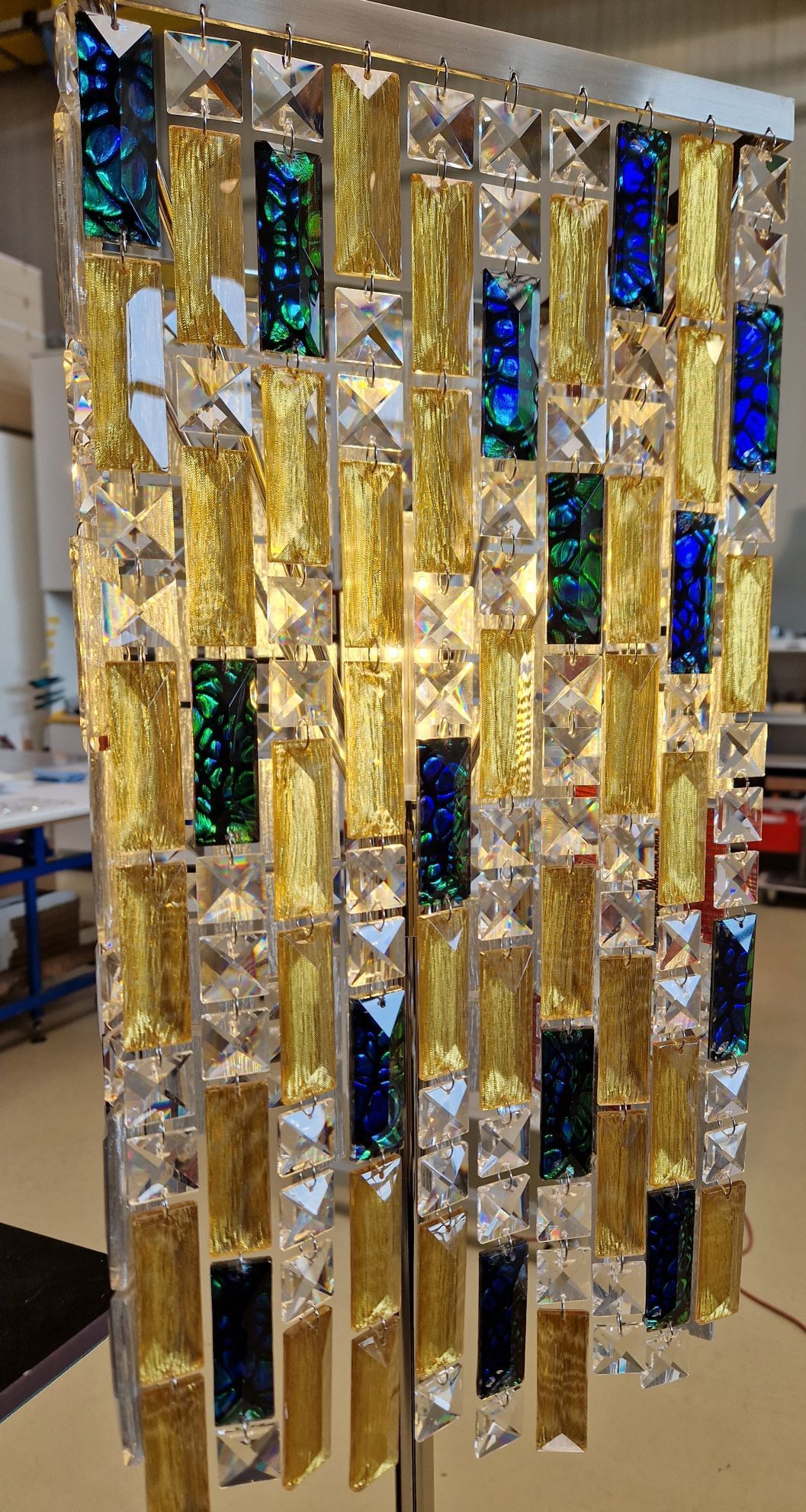 Dekoratives Hängepaneel mit rechteckigen und quadratischen Kacheln in Gold, Kristall und Blaugrün.