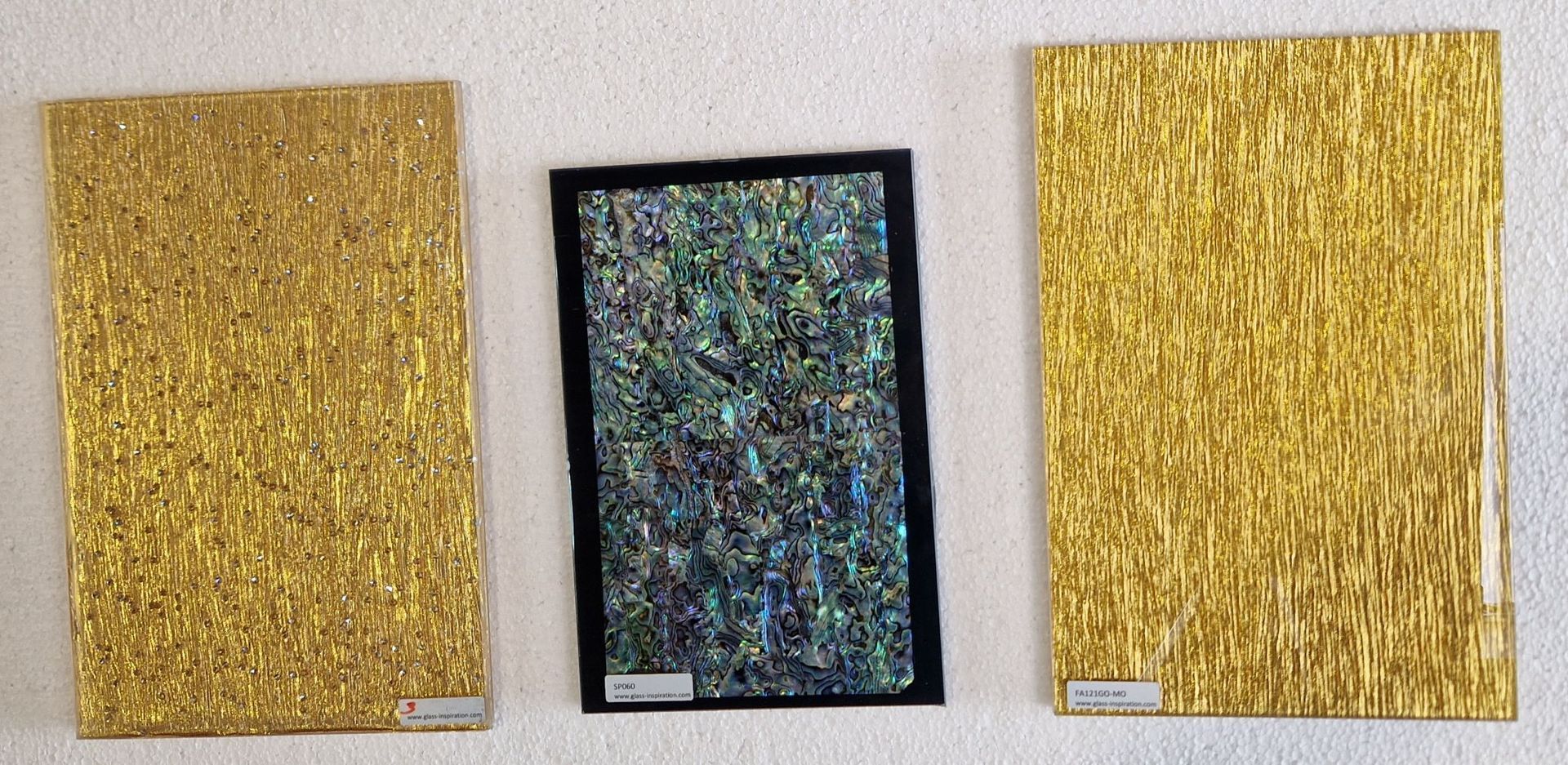 Drei strukturierte goldene Paneele mit einem schimmernden Mittelpaneel an einer weißen Wand.