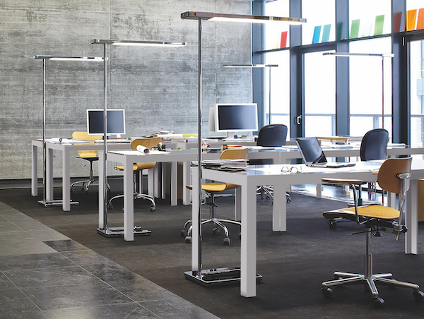 Modernes Büro mit Schreibtischen, Stühlen und Lampen. Betonwand und große Fenster. Helles, minimalistisches Design.