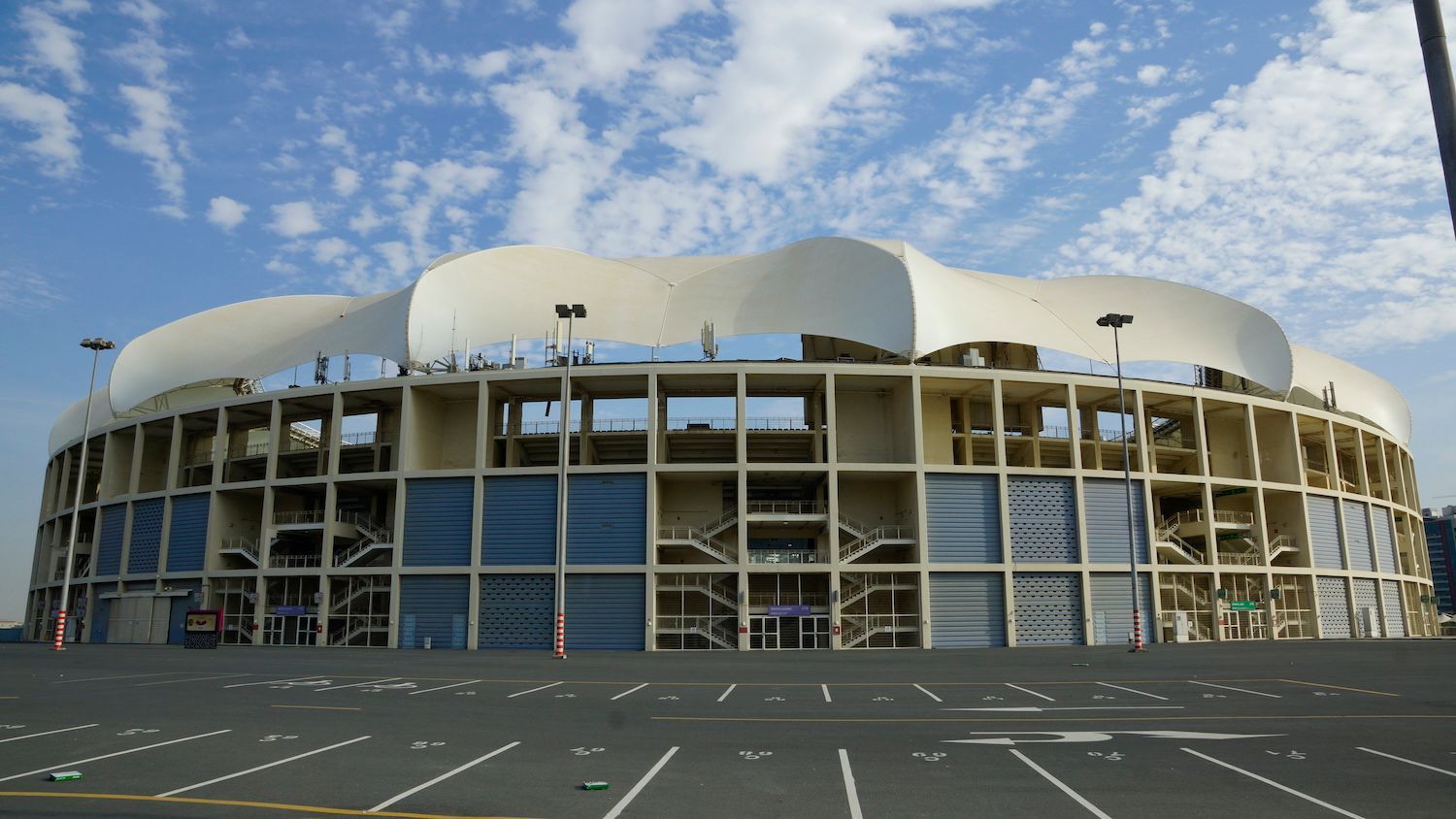 Ein helles, großes Stadion unter blauem Himmel, mit offenen Wänden und einem geschwungenen Dach.