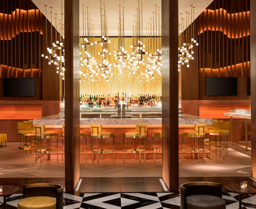 Eine luxuriöse Bar mit gelben Hockern, Marmortheke und dekorativer Beleuchtung. Der Raum ist mit Holz verkleidet.