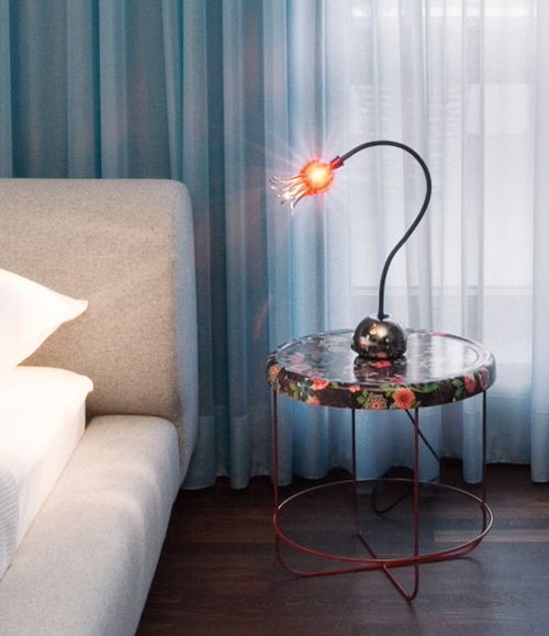 Nachttisch mit geblümter Platte und roten Beinen; Lampe mit orangefarbenem Licht.