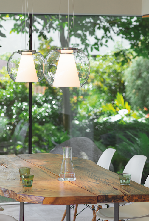 Esstisch mit Pendelleuchten und einem Fenster mit Blick ins Grüne.