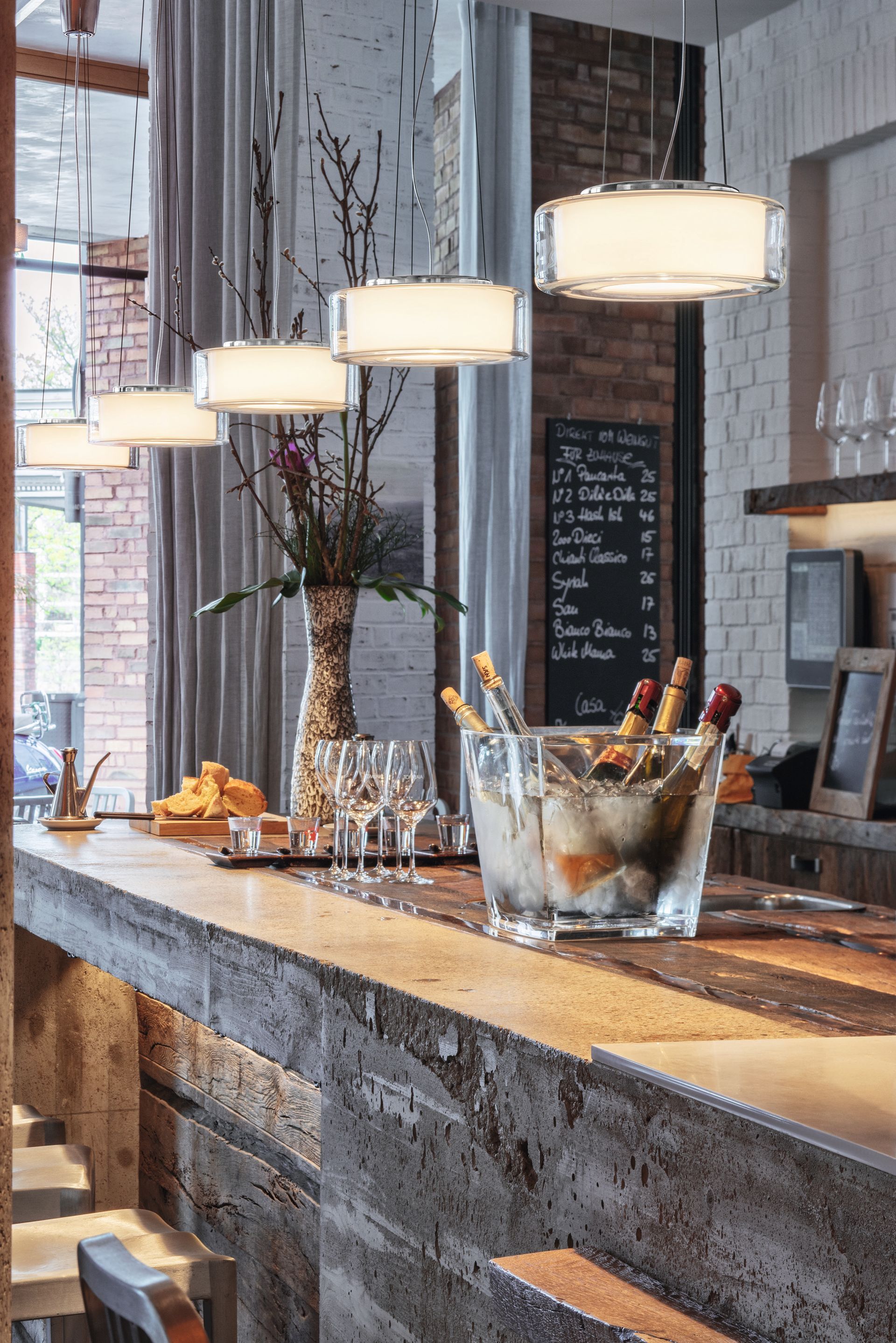Eine Bar mit Hängelampen, Holztheke, Champagnerkühler und Speisekarte an einer Ziegelwand.