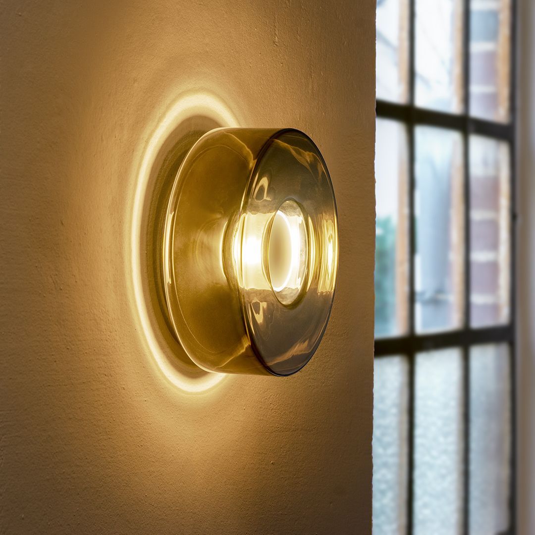 Wandleuchte aus Bernsteinglas, die die Wand in der Nähe eines Fensters mit einem warmen Schein beleuchtet.