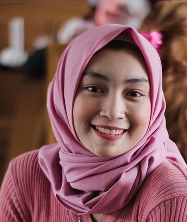 Frau im rosa Hijab lächelt und trägt einen rosa Pullover.