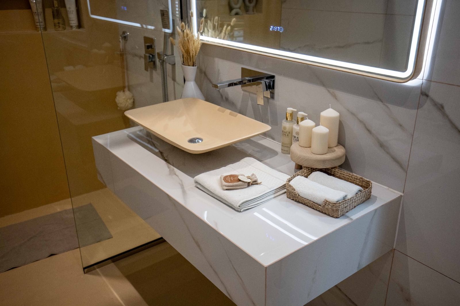 Modernes Badezimmer mit schwebendem Waschbecken, Marmorarbeitsplatte, Kerzen und beleuchtetem Spiegel.