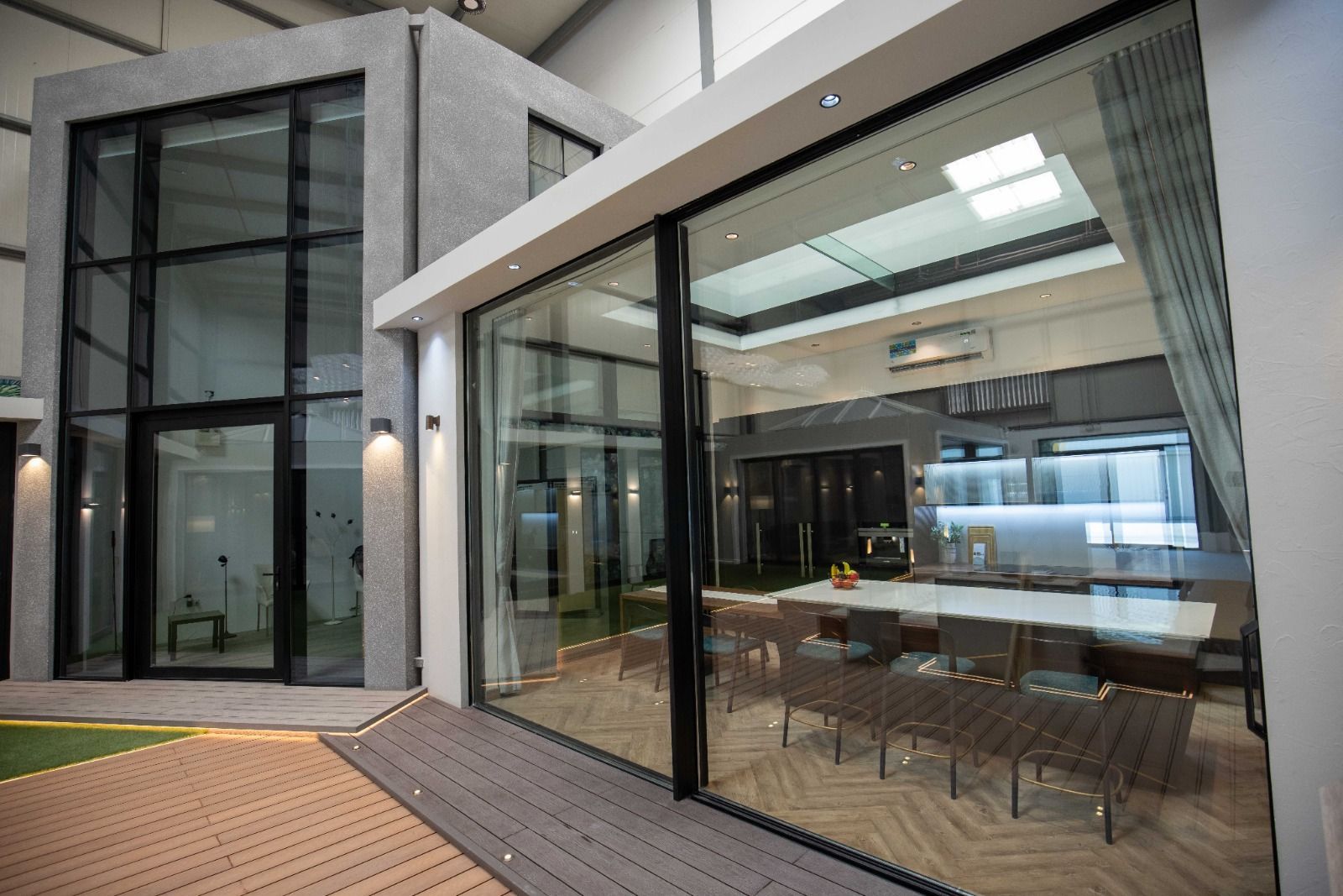 Modernes Hausäußeres mit großen Glasfenstern und -türen, die den Blick auf den Essbereich im Inneren freigeben.