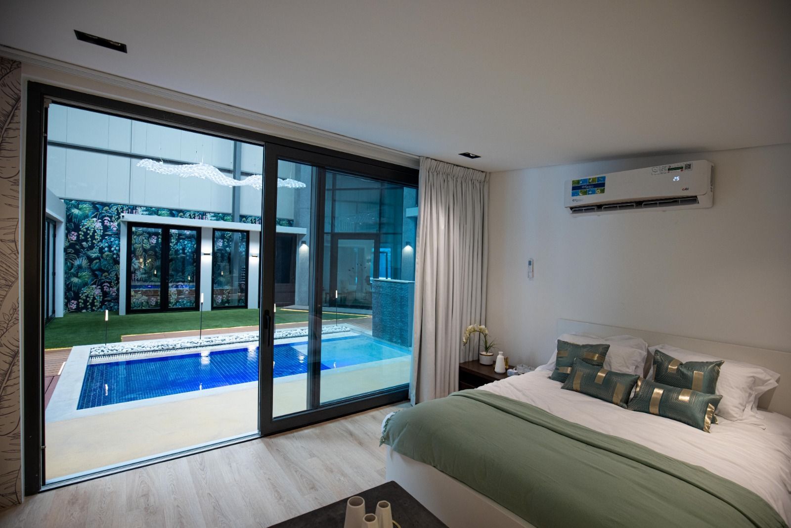 Schlafzimmer mit Poolblick: Bett, Glasschiebetüren, Pool, Terrasse, weiße Wände, heller Holzboden.