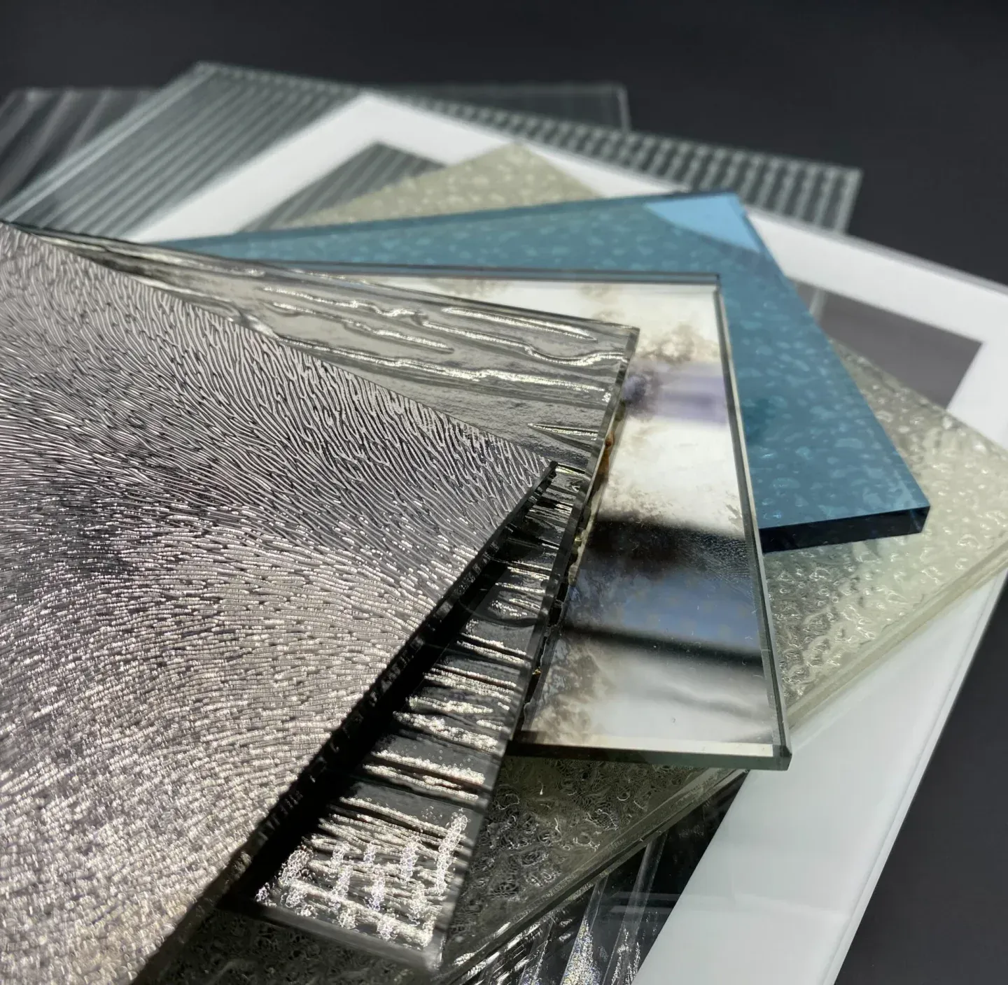 Verschiedene strukturierte Glasproben, darunter klares, mattiertes und gemustertes, übereinander gestapelt.