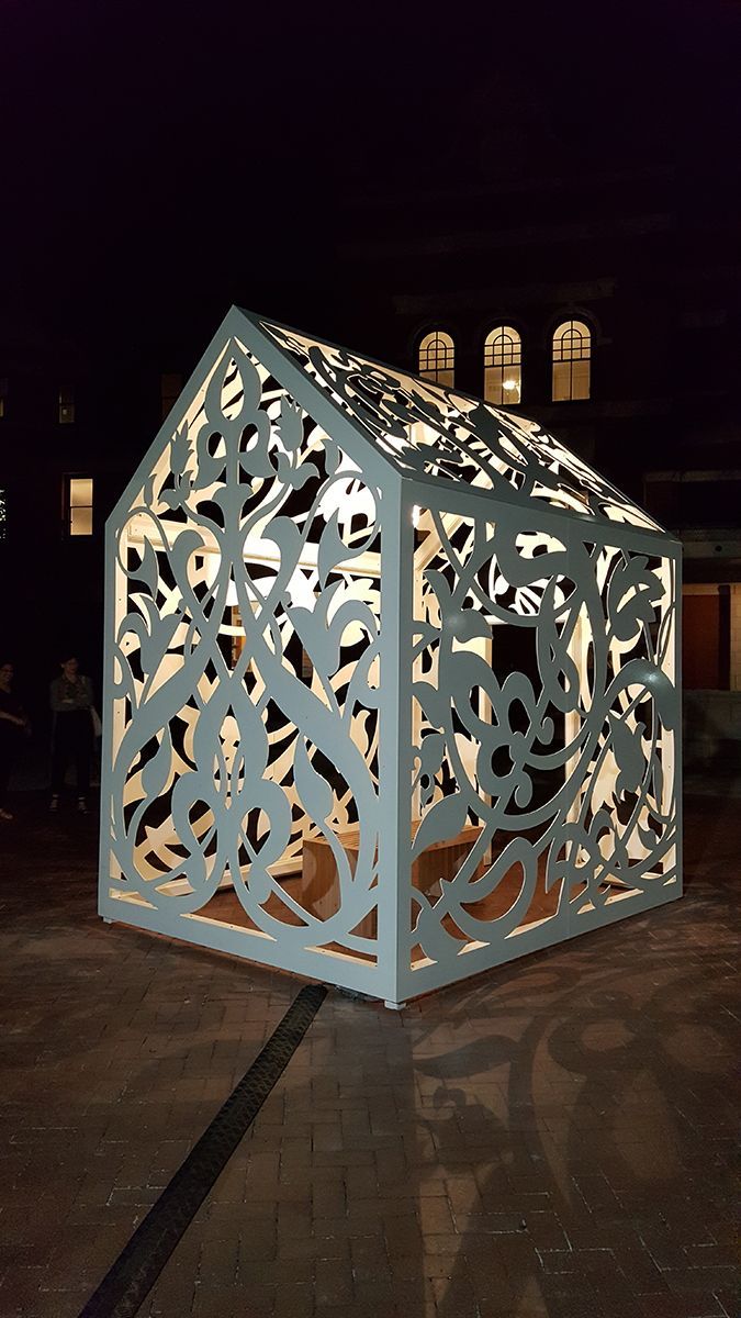 Weiße, dekorative Lichtskulptur in Form eines Hauses im Freien bei Nacht. Kunstvolle Ausschnitte leuchten in der Dunkelheit.